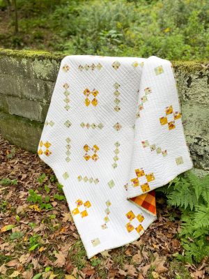 Handmade white quilt with yellow and green patterns draped over mossy wall in forest - Heart Lake Quilts design