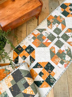 Colorful handmade quilt runner in green, orange, and white on wooden table, showcasing Heart Lake Quilts' intricate pattern design.