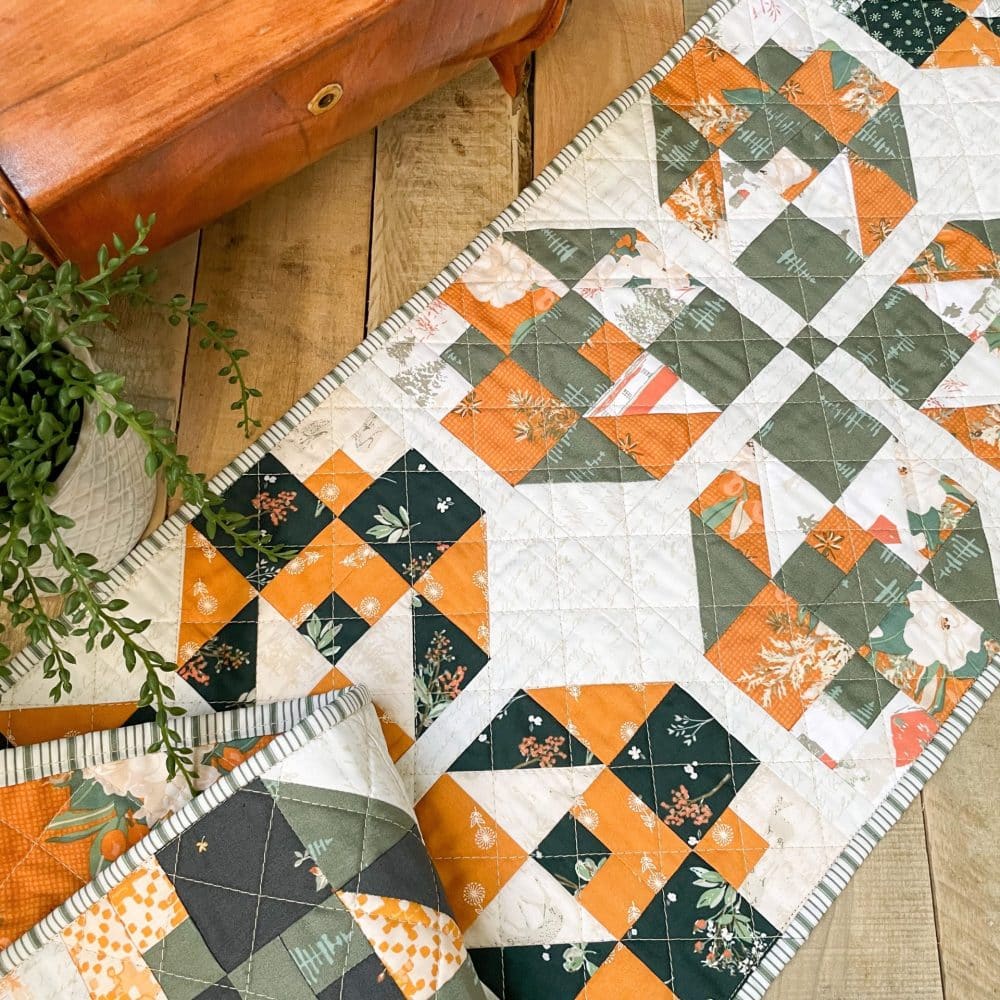 Colorful handmade quilt runner in green, orange, and white on wooden table, showcasing Heart Lake Quilts' intricate pattern design.