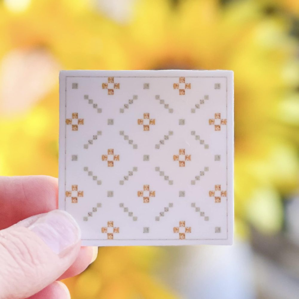 Quilter holding a small square white quilt with yellow floral pattern from Heart Lake Quilts against a blurred background.