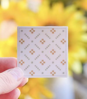 Quilter holding a small square white quilt with yellow floral pattern from Heart Lake Quilts against a blurred background.