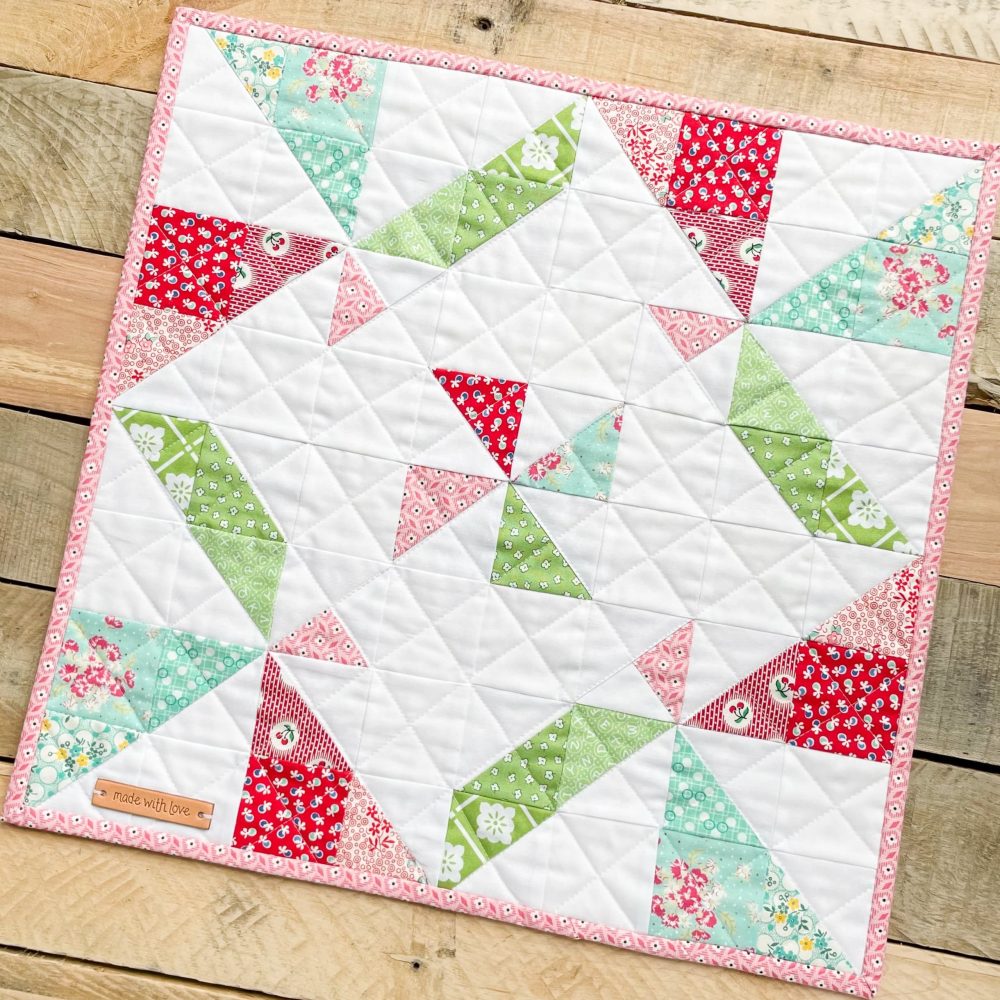 Colorful handmade quilt with geometric patterns, Heart Lake Quilts design, vibrant red, green, and pink fabrics on wood background.