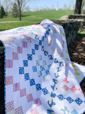 Colorful handmade quilt draped over stone wall outdoors by Heart Lake Quilts, featuring bright patchwork patterns.