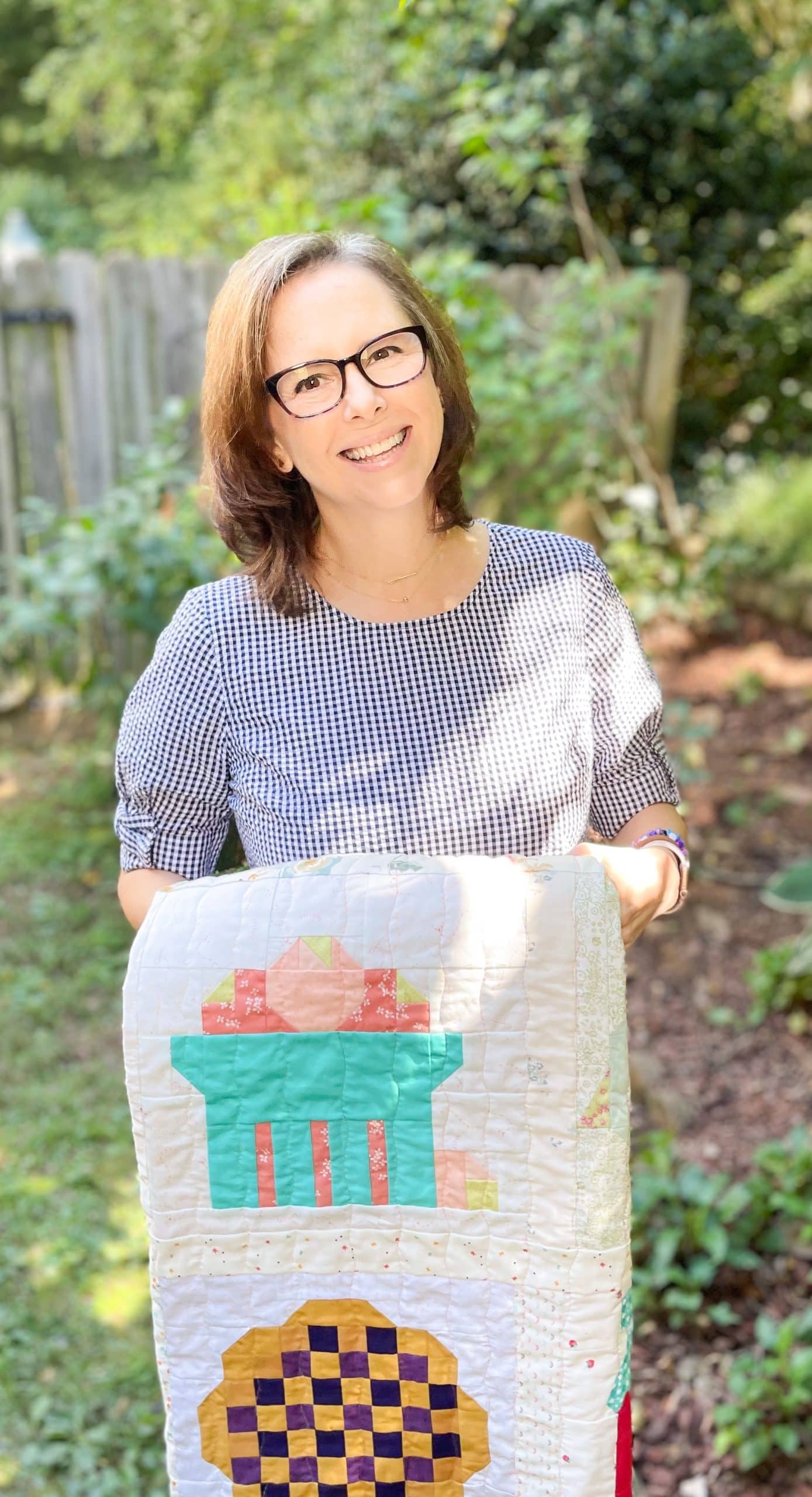 Smiling woman holding colorful quilt in garden.